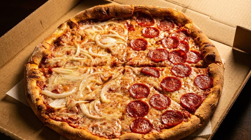 A half-pepperoni, half-onion pizza in a cardboard delivery box.