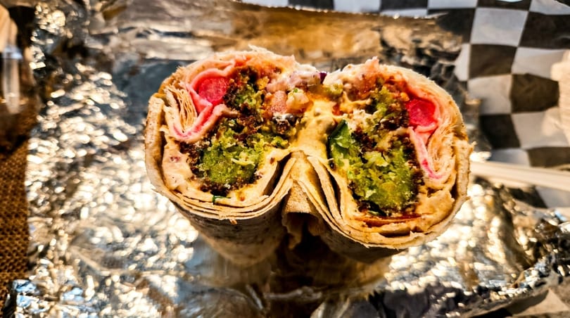A falafel wrap, cut in half, revealing green falafel, pink pickled turnips, and sauce.